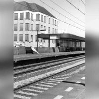 Een zomerdag rond 1995 vanaf station Houten met aan de overkant van het spoor Perron 2 (toenmalig) voor de treinen richting Geldermalsen en 's-Hertogenbosch. Op de achtergrond het kantoorgebouw Kantstede. Kantoorgebouw is later bij het gemeentehuis gevoegd voor kantoorruimte. Bron: Het Utrechts Archief, beeldbank.