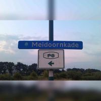 Straatnaambord 'Meidoornkade' in de oude uitvoering zoals deze in 1987 aan de lantaarnpaal is opgehangen De Meidoornkade doorsnijdt de vroegere zicht-aslaan 'Heerlijkheidspad'. Foto: Sander van Scherpenzeel.