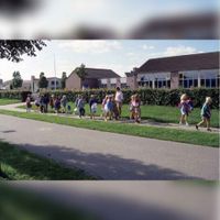 Een schoolklas loopt weg vanaf basisschool Het Schoolhuys, gezien vanaf het Rijsbrugsepad in 1990-1995. Bron: RAZU, 353.