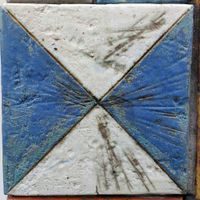 Een van de tegels aan de voorgevel van de vroegere RKBS De Bengelbongerd aan de Dijkhoeve 1. Afgebeeld vier driehoeken in elkaar geschoven als kruis in de kleuren wit en blauw. Foto: Sander van Scherpenzeel.