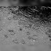 Regen vallend op de stoep in een plas. Bron: Wikipedia.