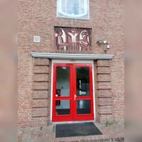 Tweede ingang van de Heilige Familie School, heden de Van Harte School aan de Loerikseweg 11a met boven de deur een afbeelding van biddende personen. In augustus 2022. Foto: Sander van Scherpenzeel.