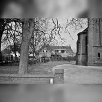 In 1979 wordt de sloop van de oude kosterswoning aan de Vlierweg 7 voorbereid. Gezien in noordelijke richting vanaf de Loerikseweg, kijkend op de achterkant van de woning. Rechts de R.K.Kerk. Collectie: Cees Verhoef.